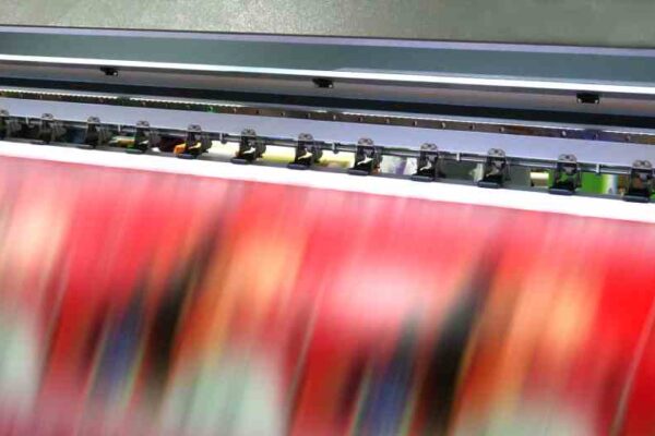 A wide-format printer rapidly prints out a blurry red print with an indistinct but brilliant design.