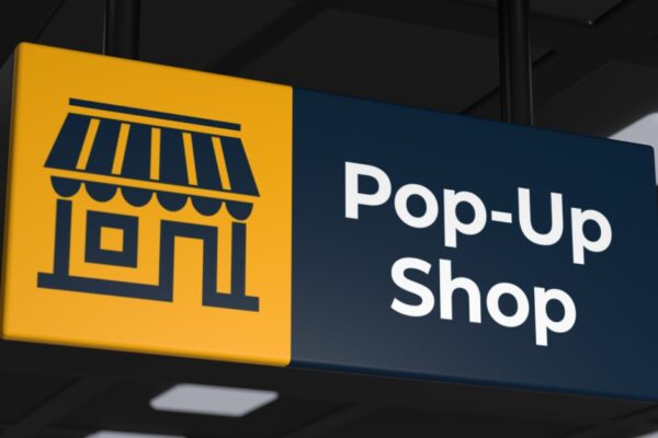 A large black and gold sign hangs from two thick wires and states "Pop-Up Shop" with a cartoon of a storefront.