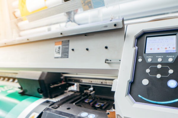 A large or wide-format plotter printer is seen running off a big colorful banner in a tight close-up.