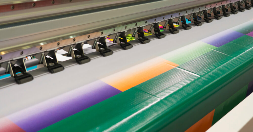 Close-up of a colorful vinyl banner emerging from a wide-format printer with a striking, blocky design.