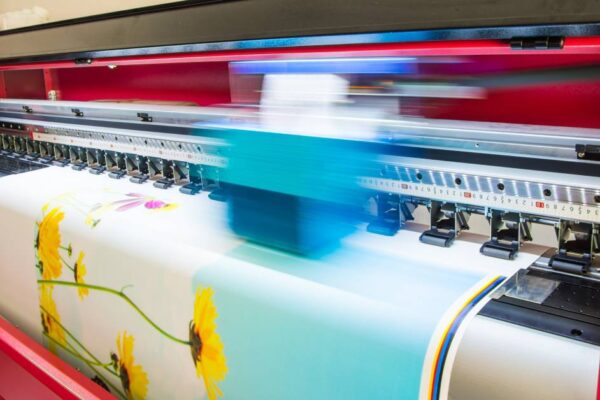 A large, red, wide-format printer is printing out an enlarged image of several yellow daisies in vibrant color.