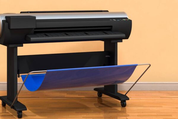 A black plotter printer with a blue catch tray standing in front of a peach-colored wall with tan wainscoting.