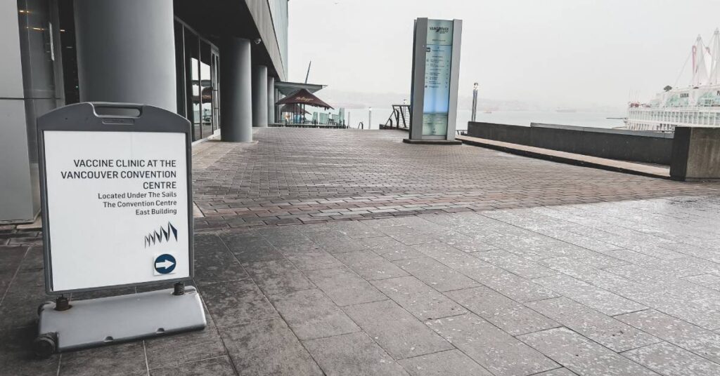 A sign is seen in front of a convention center indicating the direction to a vaccine clinic and other information.