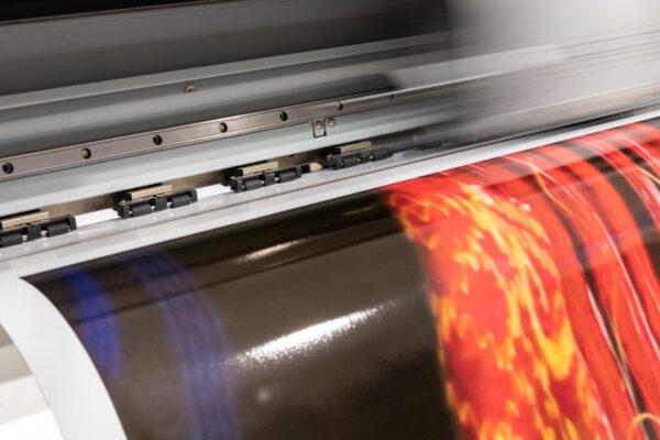 A large-format printer turns out a glossy print featuring a brightly colored red image on a dark field.