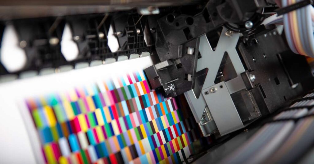 Close up on the ink heads in a printer printing out various squares in assorted bright colors in a grid.