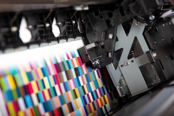 Close up on the ink heads in a printer printing out various squares in assorted bright colors in a grid.