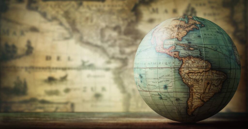 Close-up of an old-fashioned globe of the earth with an antique-looking map posted on the wall behind it.