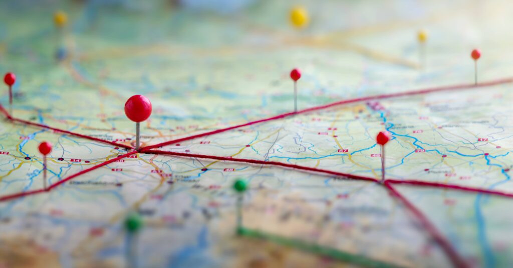 Extreme close-up on an unidentified map with multiple pushpins in different colors strung together by red thread.