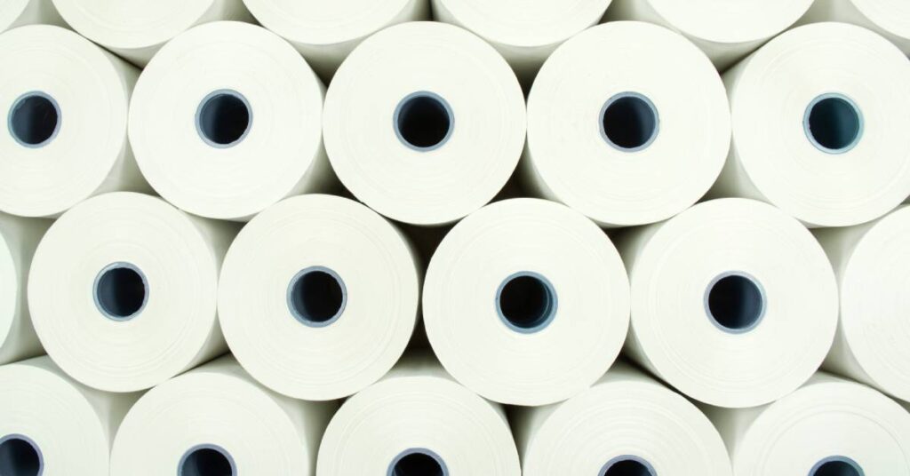 A very large stack of many different rolls of white printer paper are seen from the side, showing the spindle holes.