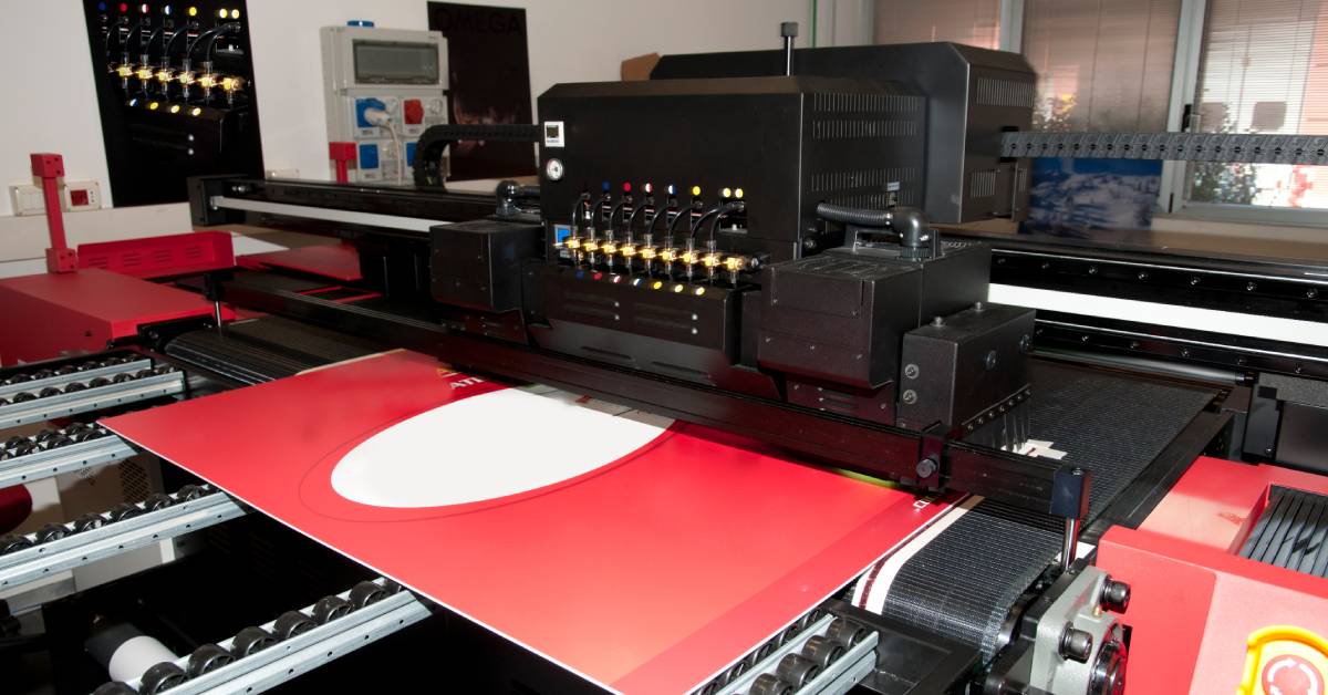 A wide-format printer in the process of printing a large red and white image. Additional equipment is in the background.