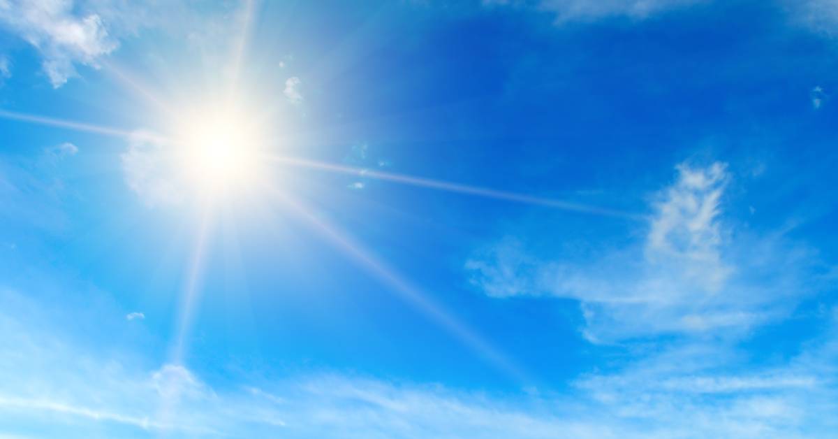 A bright blue sky with scattered clouds. The sun shines intensely, adding a starburst of light to the sky.