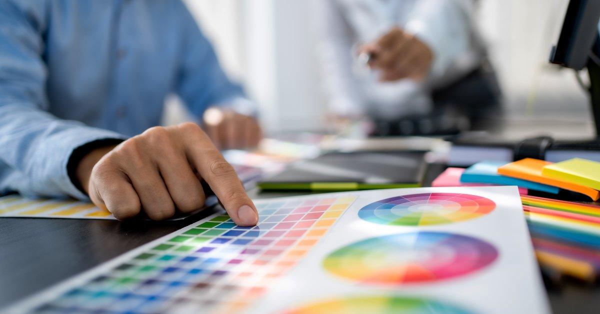 Two people in an office collaborate on a project. They point to examples on a color wheel in their meeting.