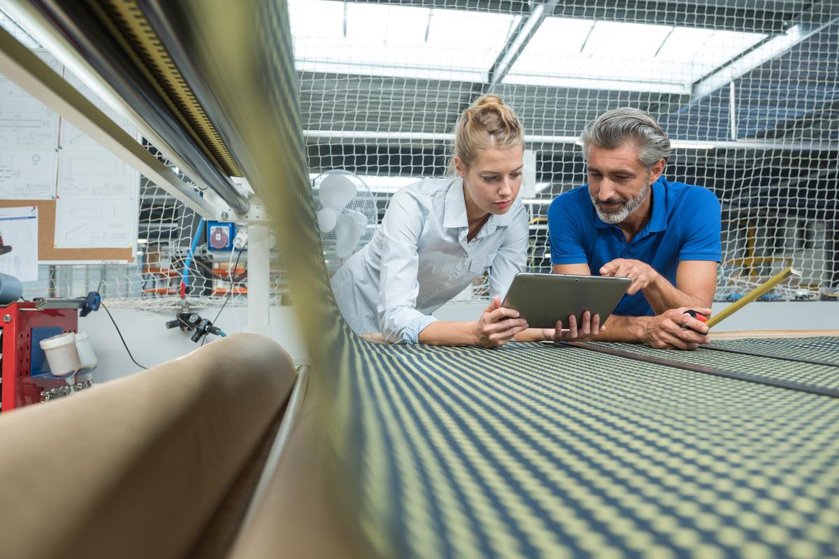 Two professionals work together to look at information on a tablet while they lean on a plotter printer.