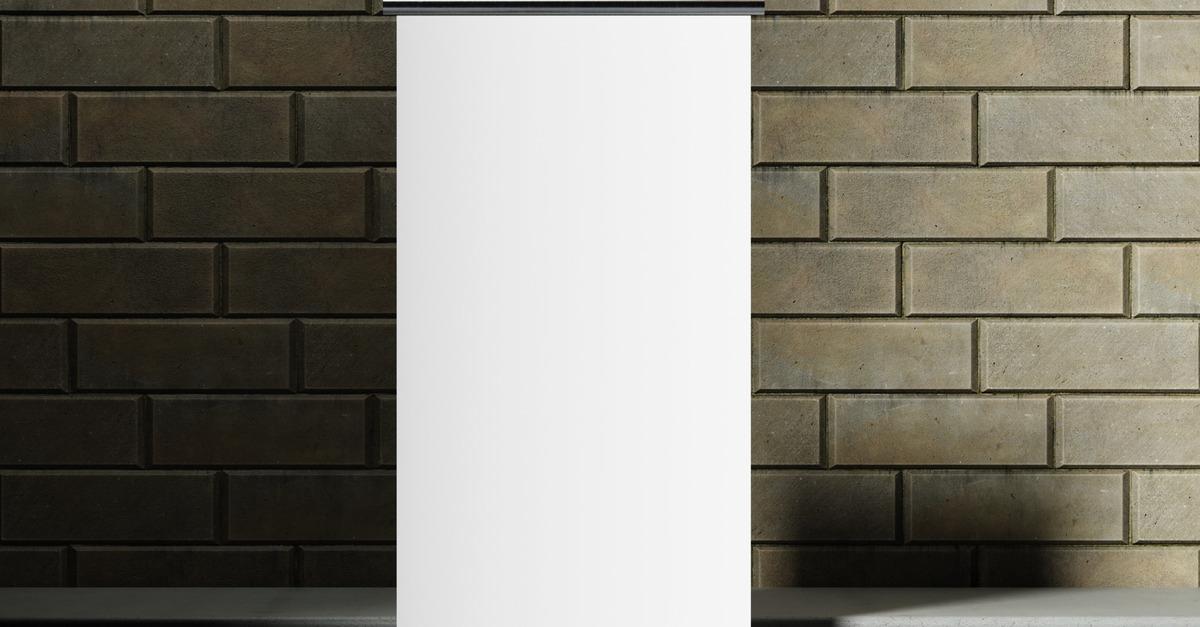 A blank white roll-up banner mock-up stands in front of a brick wall on a stone tile floor in a building.