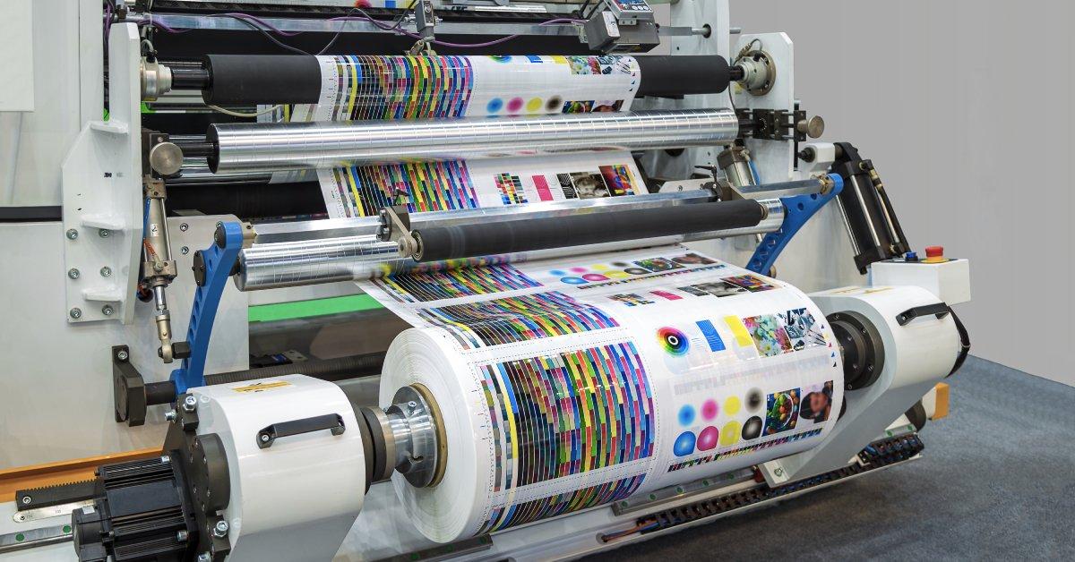 An offset printer runs a large paper roll in a production line. The intricate machine operates automatically.