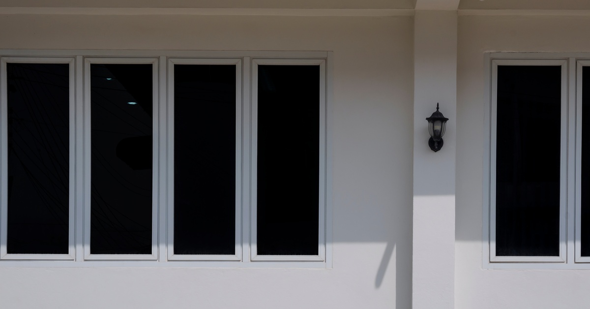 An outside view of a home's wall with several tinted glass windows. The inside of the house is not visible.